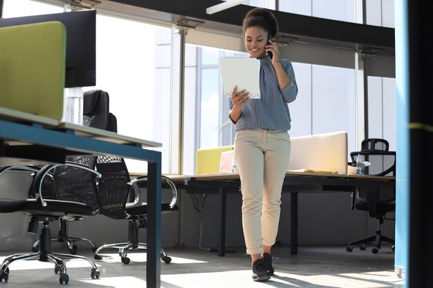 Attraente donna d'affari afroamericana che parla con i colleghi sul telefono cellulare.