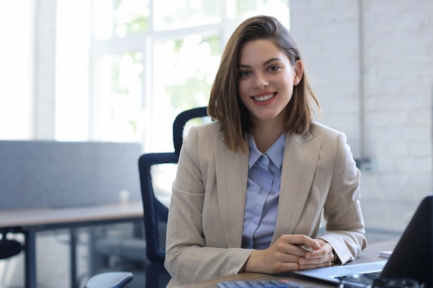 Attraente donna d'affari allegra che lavora al computer portatile in un ufficio moderno.