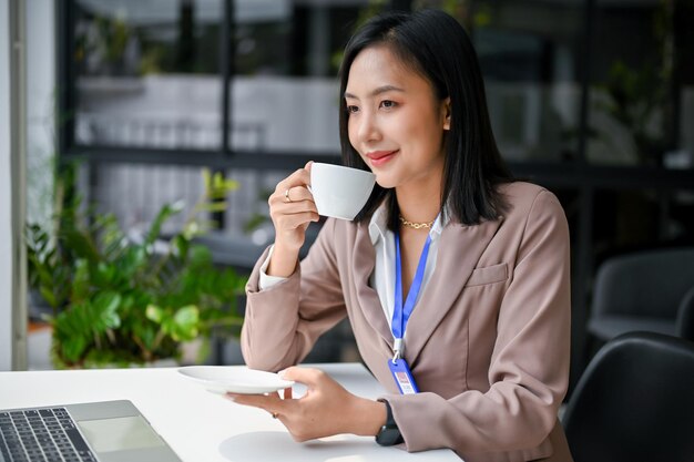 Attraente donna d'affari asiatica gode di un caffè alla sua scrivania in ufficio