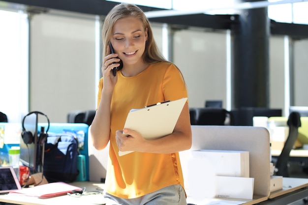 Attraente donna d'affari che parla con i colleghi al telefono cellulare mentre è seduto alla scrivania dell'ufficio.