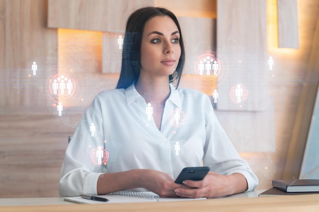 Attraente donna d'affari in camicia bianca che utilizza lo smartphone per controllare i nuovi candidati per la consulenza aziendale internazionale Icone dei social media delle risorse umane su sfondo di un ufficio moderno