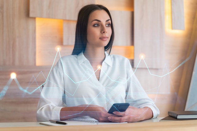 Attraente donna d'affari in camicia bianca che utilizza lo smartphone per ottimizzare la strategia di trading al fondo di finanza aziendale Ologramma grafico Forex su sfondo ufficio moderno