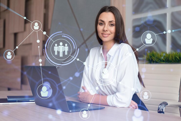 Attraente donna d'affari in camicia bianca sul posto di lavoro che lavora con il laptop per assumere nuovi dipendenti per la consulenza aziendale internazionale Icone dell'ologramma dei social media delle risorse umane sullo sfondo dell'ufficio
