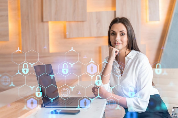 Attraente donna d'affari in camicia bianca sul posto di lavoro che lavora con il laptop per difendere la sicurezza informatica dei clienti Concetto di protezione delle informazioni dei clienti Ologramma del lucchetto sullo sfondo dell'ufficio