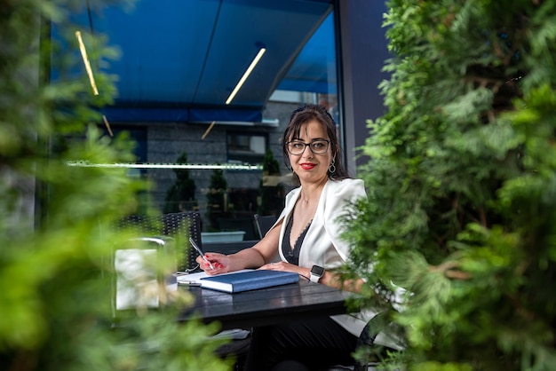 Attraente donna d'affari sta usando il suo laptop mentre è seduta all'aperto sulla terrazza del caffè