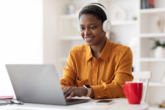 Attraente donna di colore che partecipa al webinar utilizzando laptop e auricolare