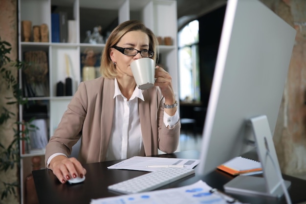 Attraente donna di mezza età che lavora in ufficio utilizzando un computer desktop contemporaneo