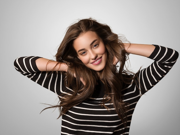 Attraente donna emotiva felice con bellissimi capelli volanti a strisce con le mani alzate che ballano il ritratto in studio