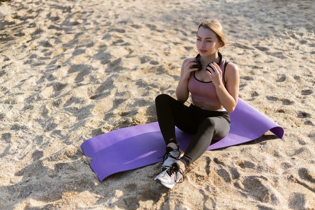 Attraente donna fitness si siede su una stuoia sulla spiaggia Stile di vita sano