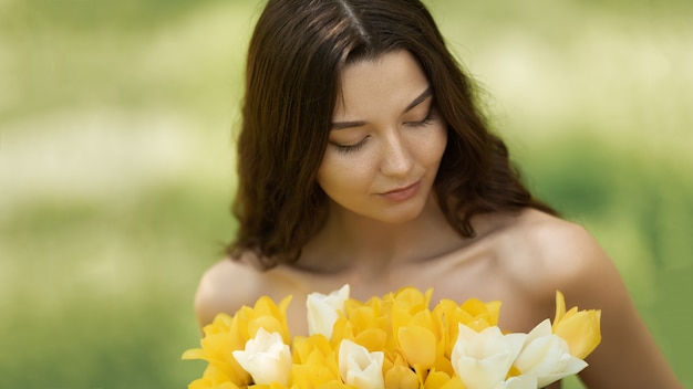 Attraente donna in abito rosso con un bouquet di fiori primaverili contro natura bokeh verde