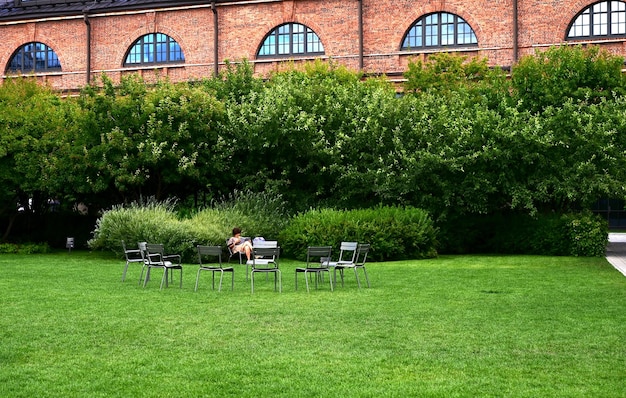 Attraente donna in maglietta a righe con occhiali e jeans neri seduta su una sedia che incrocia le gambe sull'altra Donna affascinante si gode il sole e la calda giornata all'aperto Ottenere piacere dalla vita