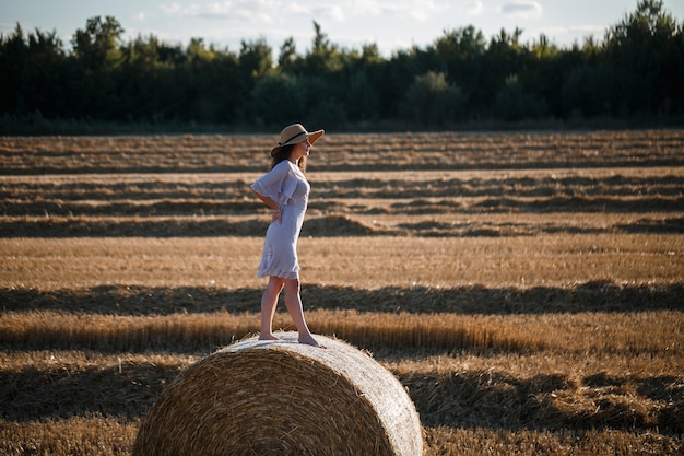 Attraente donna in posa nei campi di grano falciato con covone e cielo nel villaggio. Balle di fieno nel campo dopo il raccolto