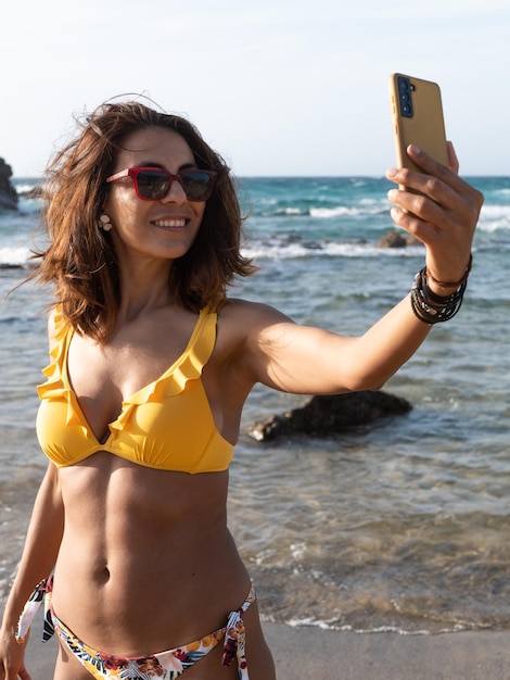 Attraente donna latina in bikini che si fa selfie sulla spiaggia