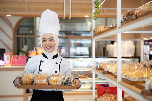 Attraente donna musulmana chef professione tenendo il vassoio sorridendo alla telecamera indossare hijab