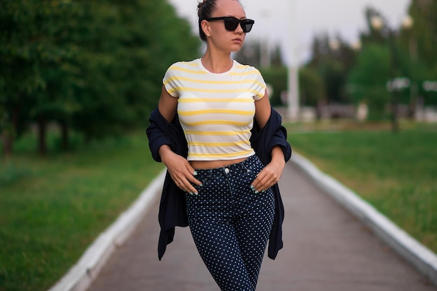 Attraente donna snella calma in camicia a righe bianche e gialle e blu con pantaloni a pois bianchi