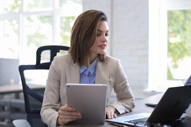 Attraente donna sorridente che lavora su un tablet in un ufficio moderno.