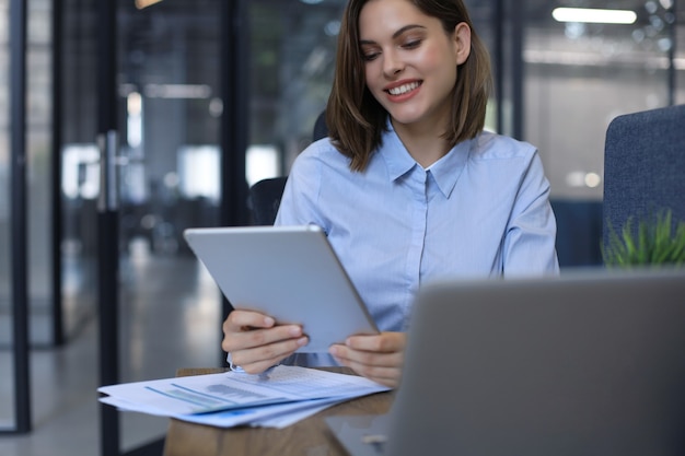 Attraente donna sorridente che lavora su un tablet in un ufficio moderno.