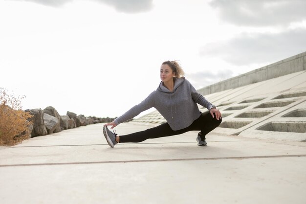 Attraente donna sportiva in abiti sportivi si allena all'aperto Riscaldare o allungare le gambe uno stile di vita sano