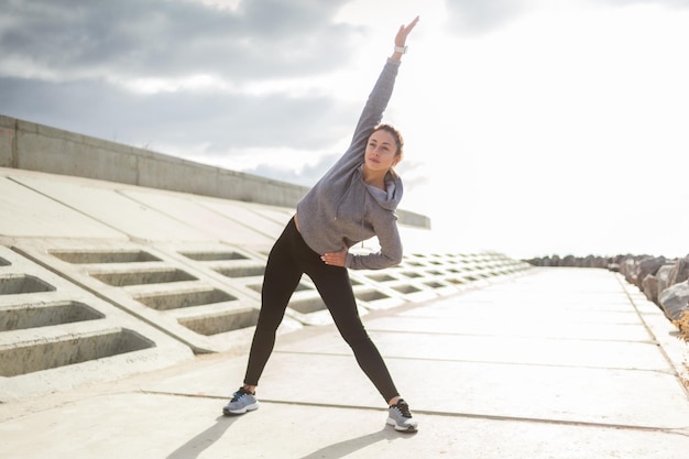 Attraente donna sportiva in abiti sportivi si allena all'aperto Riscaldare o allungare uno stile di vita sano