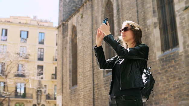 Attraente donna turistica che fa un selfie usa uno smartfone mentre cammina per strada. Godimento della libertà. Lei sorride e si gode la passeggiata.