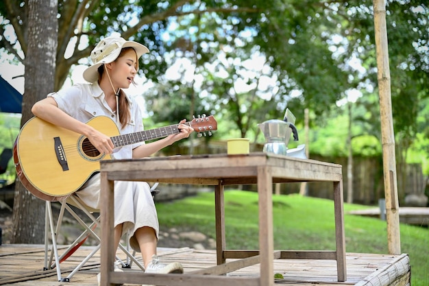 Attraente e rilassata giovane campeggiatrice asiatica che canta la sua canzone e suona la chitarra