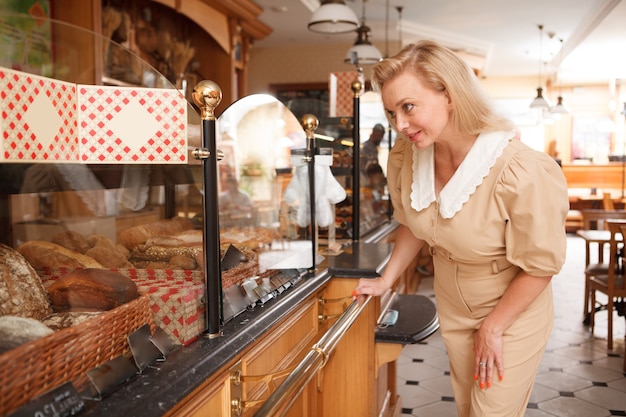 Attraente ed elegante donna matura che compra pane fresco al panificio