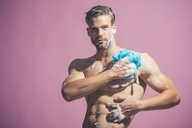 Attraente ed elegante modello macho con capelli alla moda si fa la doccia con una spugna di sapone e l'uomo nudo viene lavato