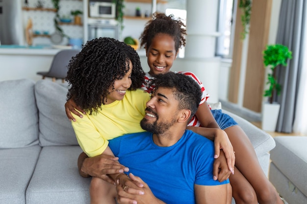 Attraente famiglia felice abbracciata madre attraente padre bello e adorabile figlia piccola seduti insieme sul divano nel soggiorno a casa sorridendo guardando la telecamera