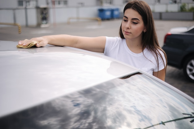 Attraente felice gioiosa autista pulisce il parabrezza della sua auto usando uno straccio nell'autolavaggio self-service