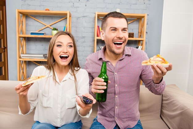 Attraente felice giovane uomo e donna guardando la tv con birra e pizza