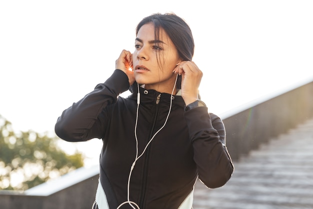 Attraente fitness donna che indossa abiti sportivi che esercitano all'aperto, ascoltando musica con gli auricolari