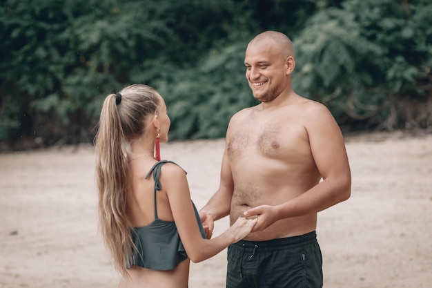 Attraente giovane coppia alla moda in abiti bianchi cammina sulla spiaggia e si tiene per mano. La bella bionda con i capelli lunghi e un uomo calvo sono in vacanza. Phuket. Tailandia.