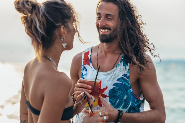 Attraente giovane coppia con cocktail alcolici che camminano sulla spiaggia