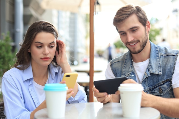 Attraente giovane coppia innamorata che beve caffè seduti al tavolino del bar all'aperto, utilizzando il telefono cellulare.