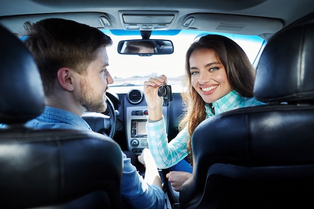 Attraente giovane coppia seduta nella nuova automobile e guardando la fotocamera e sorridente, l'acquisto di una nuova auto, tenendo le chiavi.