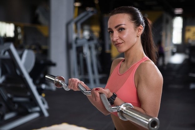 Attraente giovane culturista femminile che si allena con il bilanciere, facendo riccioli per bicipiti in palestra