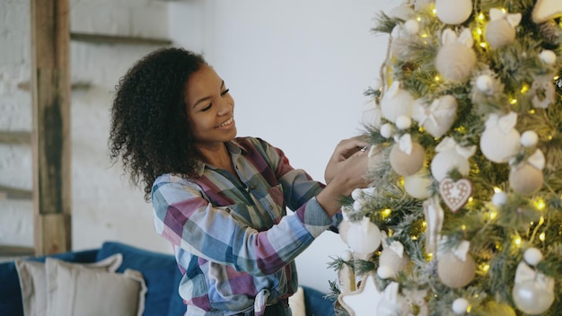 Attraente giovane donna africana che decora l'albero di Natale a casa preparandosi per la celebrazione di Natale