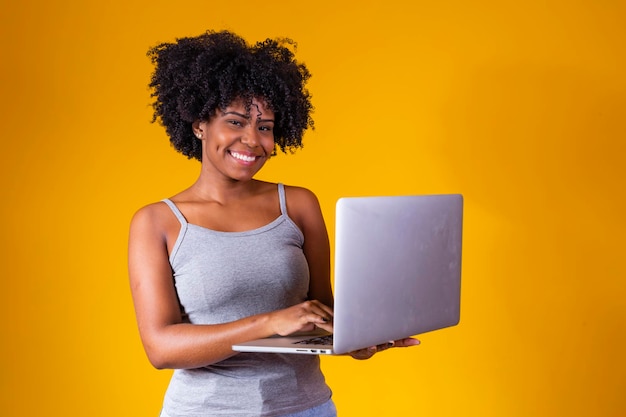 Attraente giovane donna africana che indossa abiti casual in piedi isolato su sfondo giallo utilizzando il computer portatile