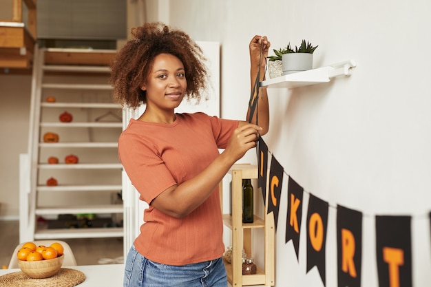 Attraente giovane donna afro-americana che decora la stanza con la ghirlanda per la festa di Halloween, copia dello spazio