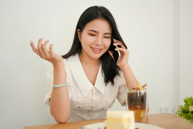 Attraente giovane donna asiatica che parla al telefono bianca la sua amica mentre è seduto al caffè