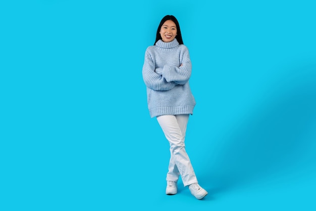 Attraente giovane donna asiatica in maglione caldo in posa sul blu