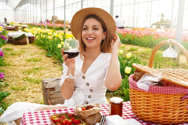 Attraente giovane donna avente antipasto tra fiori di tulipano Raccolto fresco con picnic e vino rosso in campagna in primavera