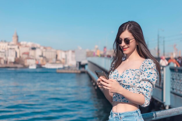 Attraente giovane donna bruna che guarda al telefono cellulare con i suoi occhiali da sole nello spazio della copia di Istanbul