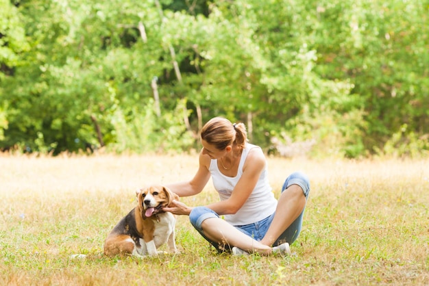 Attraente giovane donna che accarezza il suo cane di razza pura seduto all'aperto sull'erba verde