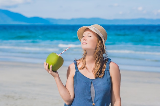 Attraente giovane donna che beve acqua di cocco sulla spiaggia