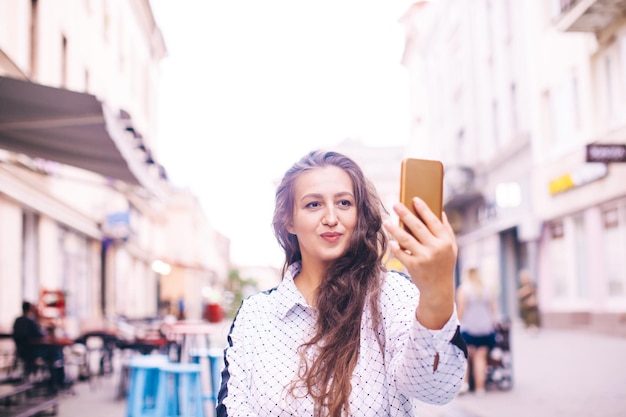 Attraente giovane donna che indossa una camicia bianca si fa un selfie in una strada della città europea