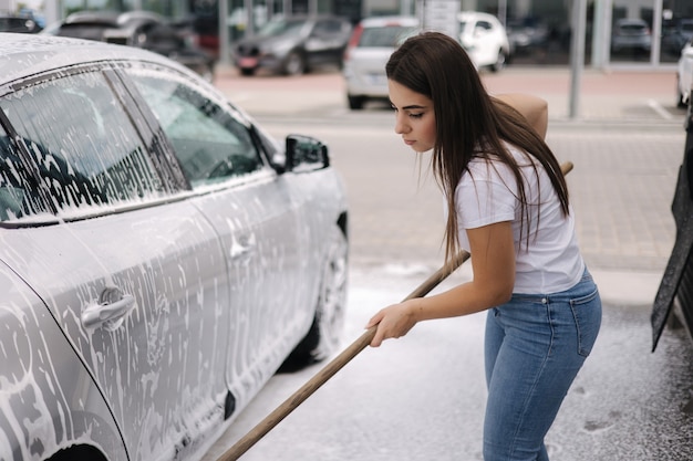 Attraente giovane donna che lava la sua auto con shampoo e spazzole femmina lava automobile con schiuma