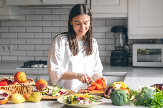 Attraente giovane donna che taglia le verdure per insalata in cucina