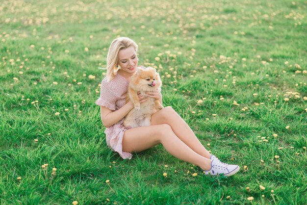 Attraente giovane donna che tiene spitz di cane fuori e sorride alla macchina fotografica, camminando nel parco.