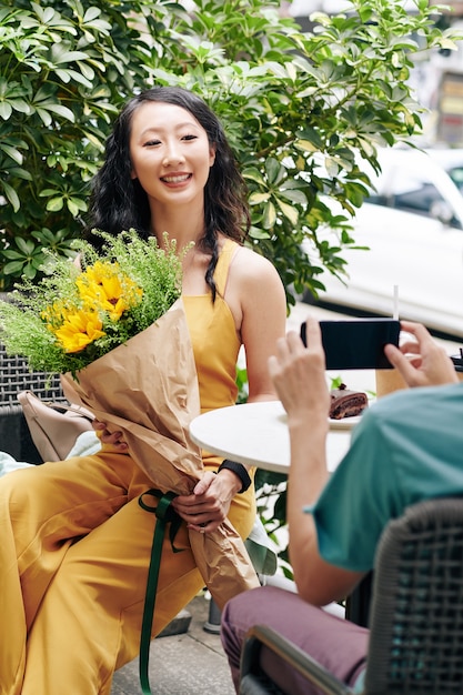 Attraente giovane donna cinese in tuta gialla in posa per una foto con bouquet di fiori dal fidanzato